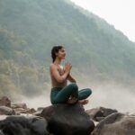 “슬기로운 아침 루틴으로 활기찬 하루 열기” – 건강 트렌드와 함께하는 실천법 a woman sitting on top of a rock next to a river