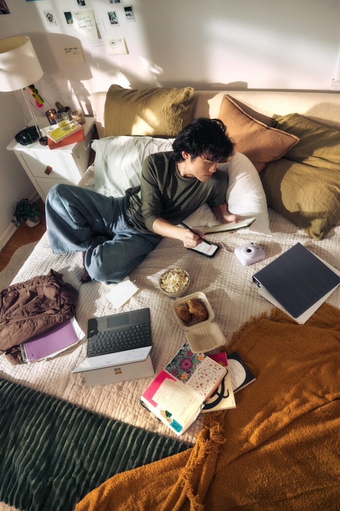 Photo by Microsoft Copilot Young man on bed with laptop and snacks