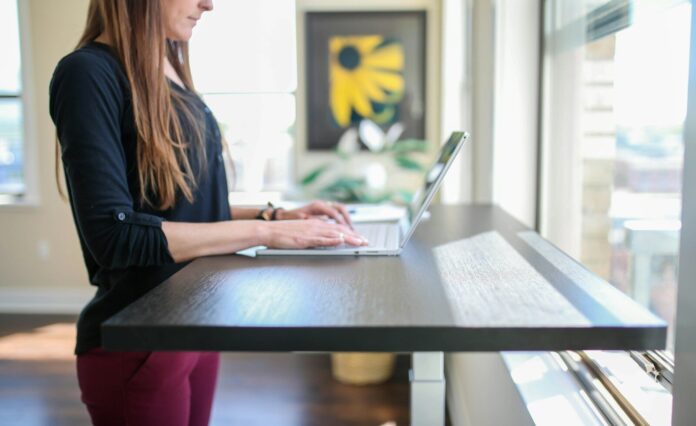 Photo by TheStandingDesk woman in black shirt sitting at the table using macbook